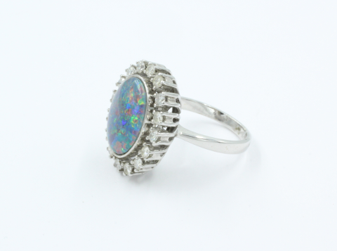 Een 14 karaats witgouden ring waarin een ovale opaal triplet ( onyx, opaal, en bergkristal) 15 bij 11 mm . Om de opaal 16 briljanten van elk 0.03 ct . Bruto 7.2 gram 